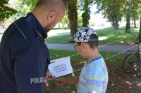 Obraz przedstawia policjanta wraz z dzieckiem na pikniku edukacyjnym