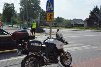 Obraz przedstawia funkcjonariusza ruchu drogowego i motocykl kontrolującego przejście dla pieszych w rejonie szkół