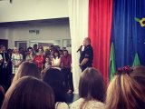 Obraz przedstawia dzielnicowego przemawiającego  na inauguracji roku szkolnego 2019/2020 w szkole w Czyżewie  w towarzystwie dzieci