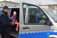 Obraz przedstawia dzieci oglądające radiowóz i policjantka, który omawia poszczególne elementy wyposażenia