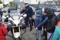 Obraz przedstawia policjanta ruchu drogowego, który pokazuje dzieciom motocykl