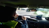 Obraz przedstawia policjanta &quot;drogówki&quot; za kierownicą radiowozu