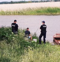 Obraz przedstawia policjantów nad rzeką w Waniewie kontrolujących osoby