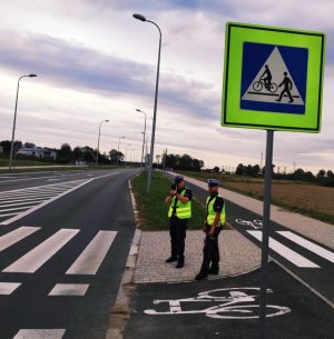 Obraz przedstawia policjantów pełniących służbę w pobliżu przejść  dla pieszych