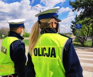 Obraz przedstawia dwoje policjantów wydziału ruchu drogowego w maseczkach stojących przed przejściem dla pieszych w Wysokiem Mazowieckiem