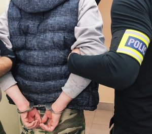 Obraz przedstawia dłonie zatrzymanego w kajdankach i ramie policjanta