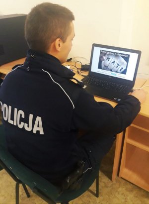 Obraz przedstawia dzielnicowego z Posterunku Policji w Czyżewie siedzącego przed laptopem