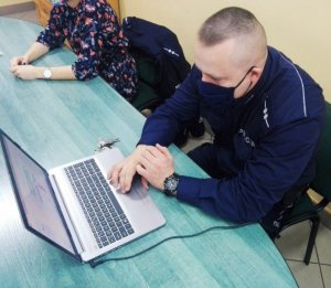 Obraz przedstawia policjanta siedzącego przed laptopem