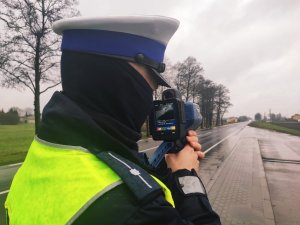 Obraz przedstawia policjanta dokonującego pomiaru prędkości