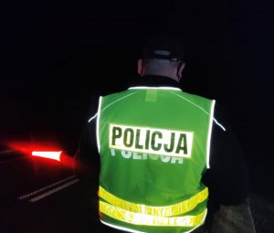 Obraz przedstawia policjanta trzymającego tarczę do zatrzymywania pojazdów