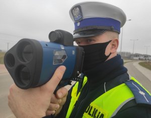 Obraz przedstawia policjanta trzymającego w ręce urządzenie do pomiaru prędkości
