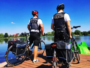 obraz przedstawia policjantów na rowerach na tle zbiornika wodnego
