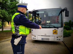 obraz przedstawia policjanta w kamizelce odblaskowej, w tle autobus