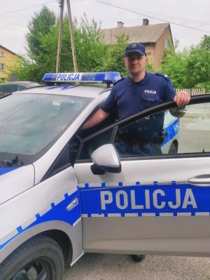 obraz przedstawia policjanta stojącego przy radiowozie