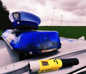 obraz przedstawia czapkę policjanta usytuowaną na radiowozie a obok urządzenie do pomiaru stanu trzeźwości