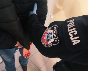 obraz przedstawia ramię policjanta z naszywką Policja Posterunek Policji Czyżew trzymające ramię mężczyzny w czarnej kurtce