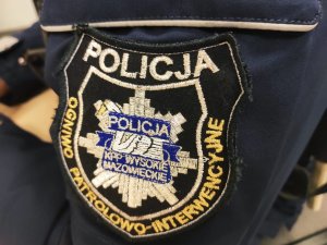 obraz przedstawia ramię policjanta z naszywką na której widniej napis Komenda Powiatowa Policji w Wysokiem Mazowieckiem