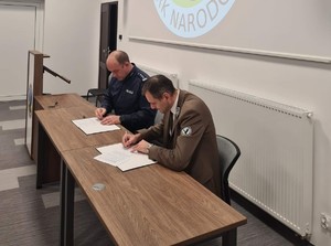 obraz przedstawia Komendanta Powiatowego Policji oraz Dyrektora Narwiańskiego Parku Narodowego podpisujących porozumienie