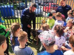 obraz przedstawia policjantów na spotkaniu z grupą dzieci, policjanci pokazują psa służbowego