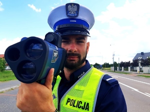 obraz przedstawia policjanta trzymającego urządzenie do pomiaru prędkości