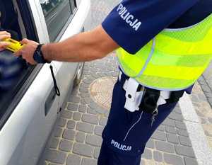 obraz przedstawia policjanta trzymającego urządzenie do badania stanu trzeźwości