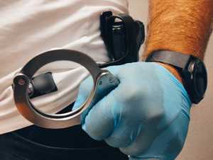 obraz przedstawia dłoń policjanta w rękawiczce trzymającą kajdanki