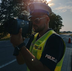 obraz przedstawia policjanta Wydziału Ruchu Drogowego trzymającego urządzenie do pomiaru prędkości