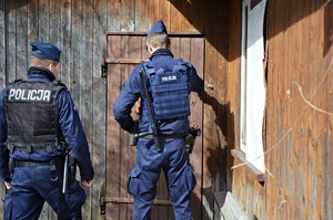 obraz przedstawia policjantów na tle drewnianego budynku