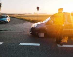 obraz przedstawia policjanta dokonującego badania stanu trzeźwości kierowcy, w tle radiowóz