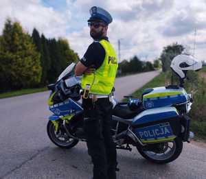 obraz przedstawia policjanta stojącego przy motocyklu